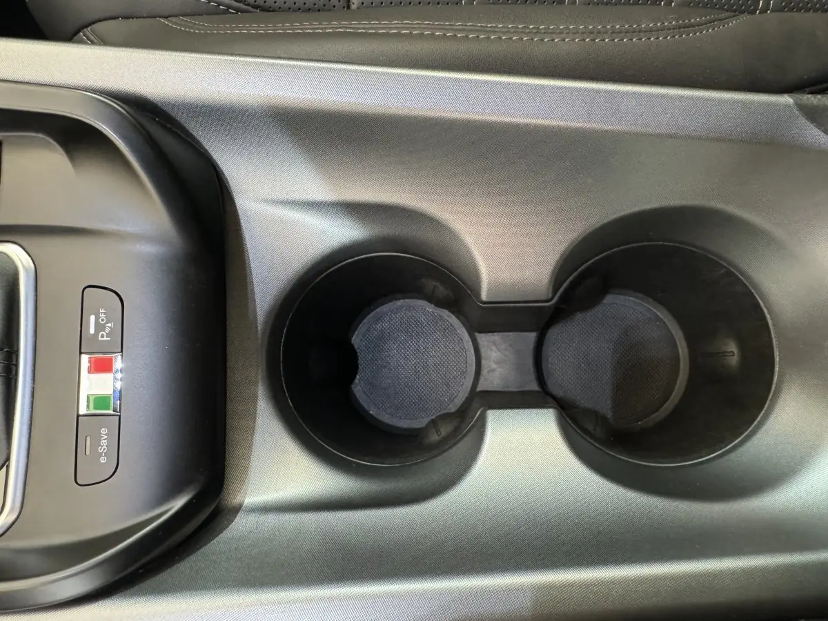 Gros plan sur les porte-gobelets noirs et les boutons de contrôle avec drapeau italien dans la console centrale d'une Alfa Romeo Tonale rouge.