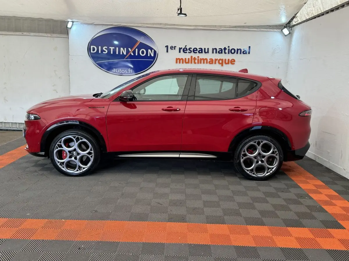 Profil droit d'un Alfa Romeo Tonale rouge 2023 avec jantes originales et détails noirs contrastants dans un showroom.