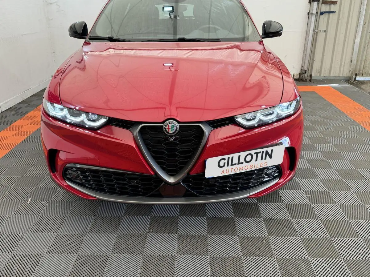 Vue frontale rapprochée de l'Alfa Romeo Tonale rouge avec calandre triangulaire et phares LED allumés.