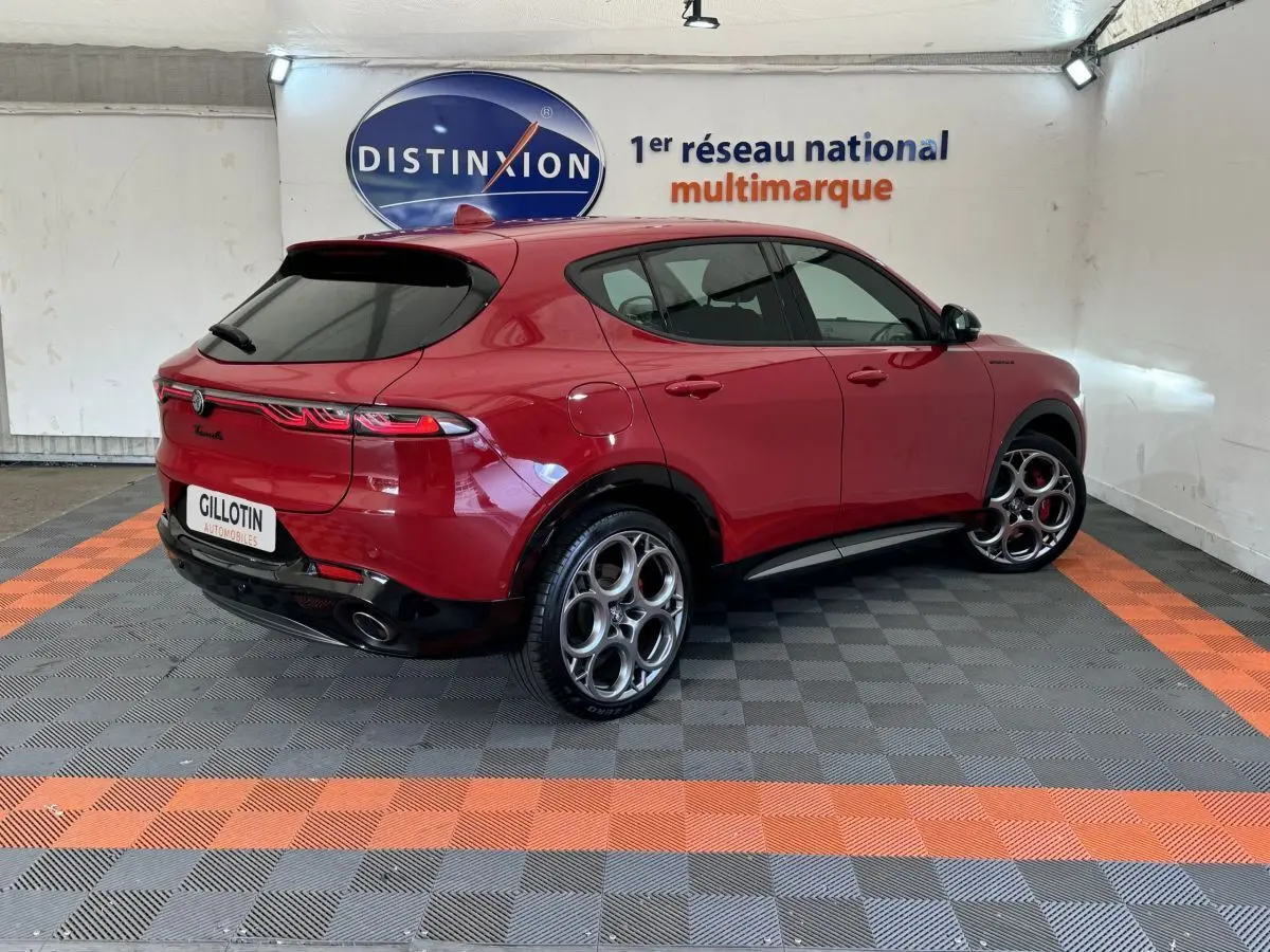 Vue 3/4 arrière droite d'une Alfa Romeo Tonale rouge avec jantes distinctives et feux arrière LED en showroom