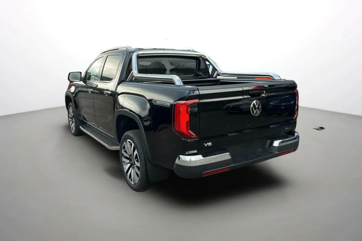 Volkswagen Amarok simple cabine noir 2025, vue 3/4 arrière droit, avec barres de caisse chromées et logo V6 visible.