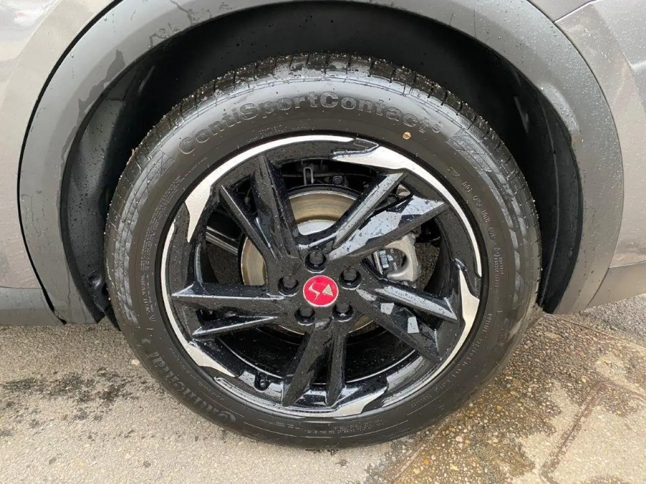 Gros plan sur la jante noire brillante avec logo DS rouge du DS7 Crossback gris platinium, roue avant droite humide.