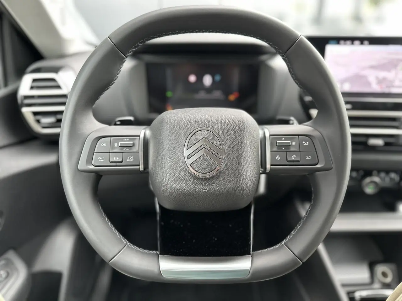 Gros plan sur le volant cuir noir de la Citroën C4 NV Hybrid 2025 avec commandes intégrées et logo central chrome.