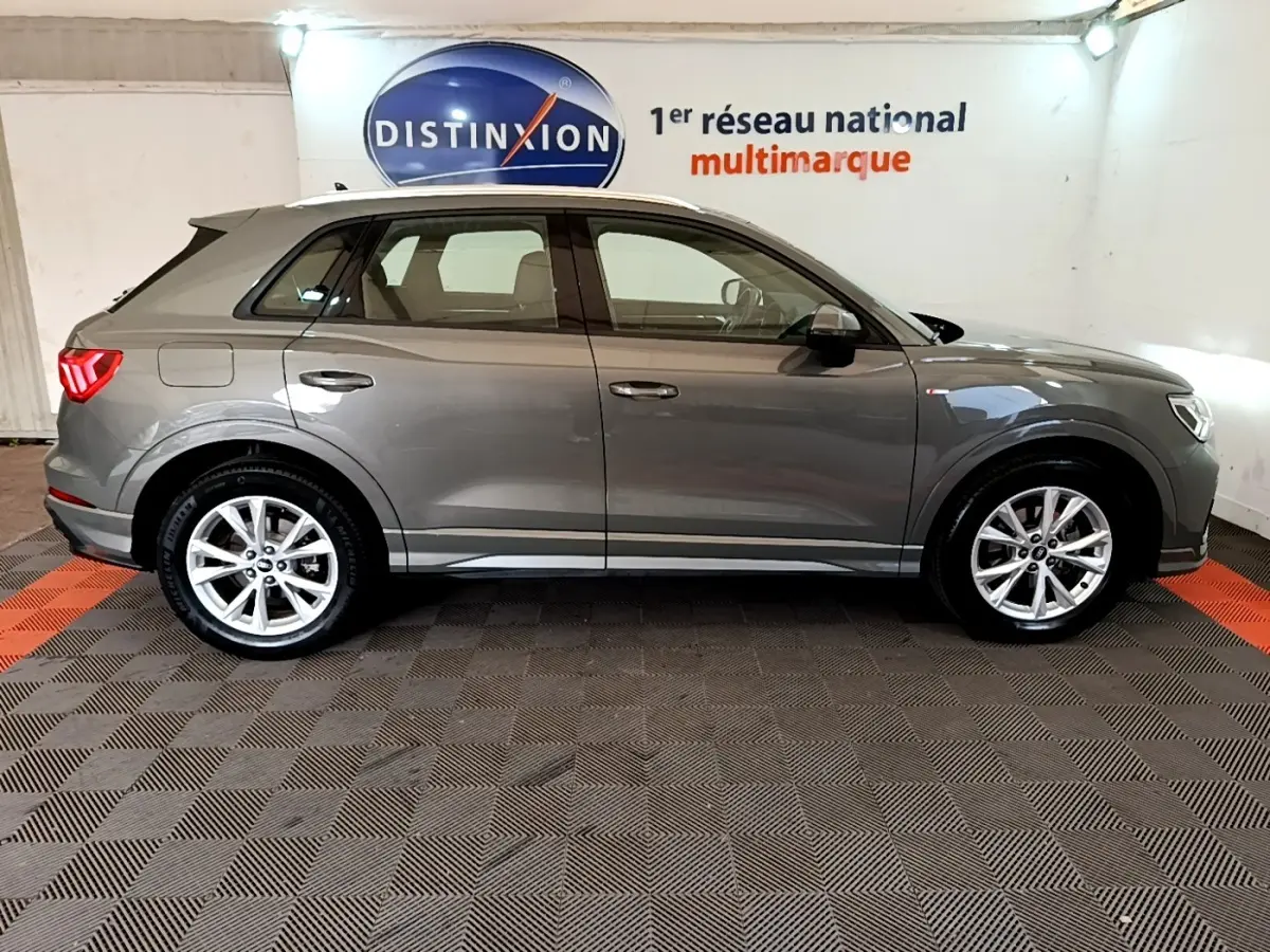 Audi Q3 35 TFSI S Line gris foncé vue de profil côté gauche dans un showroom avec sol à damier noir et rouge.