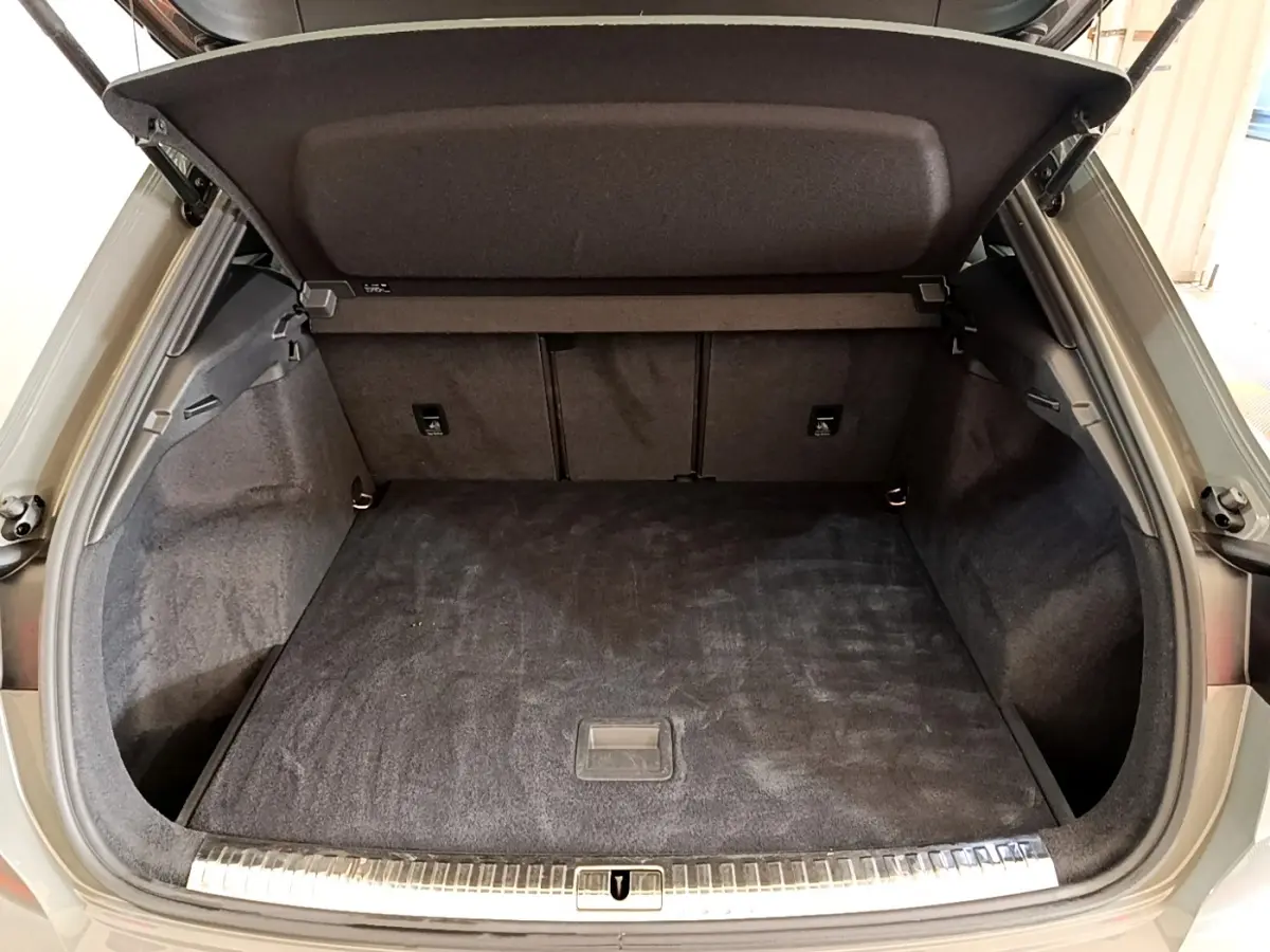 Coffre ouvert vu de l'arrière d'un Audi Q3 gris foncé, avec tapis de sol noir et habillage intérieur sombre.