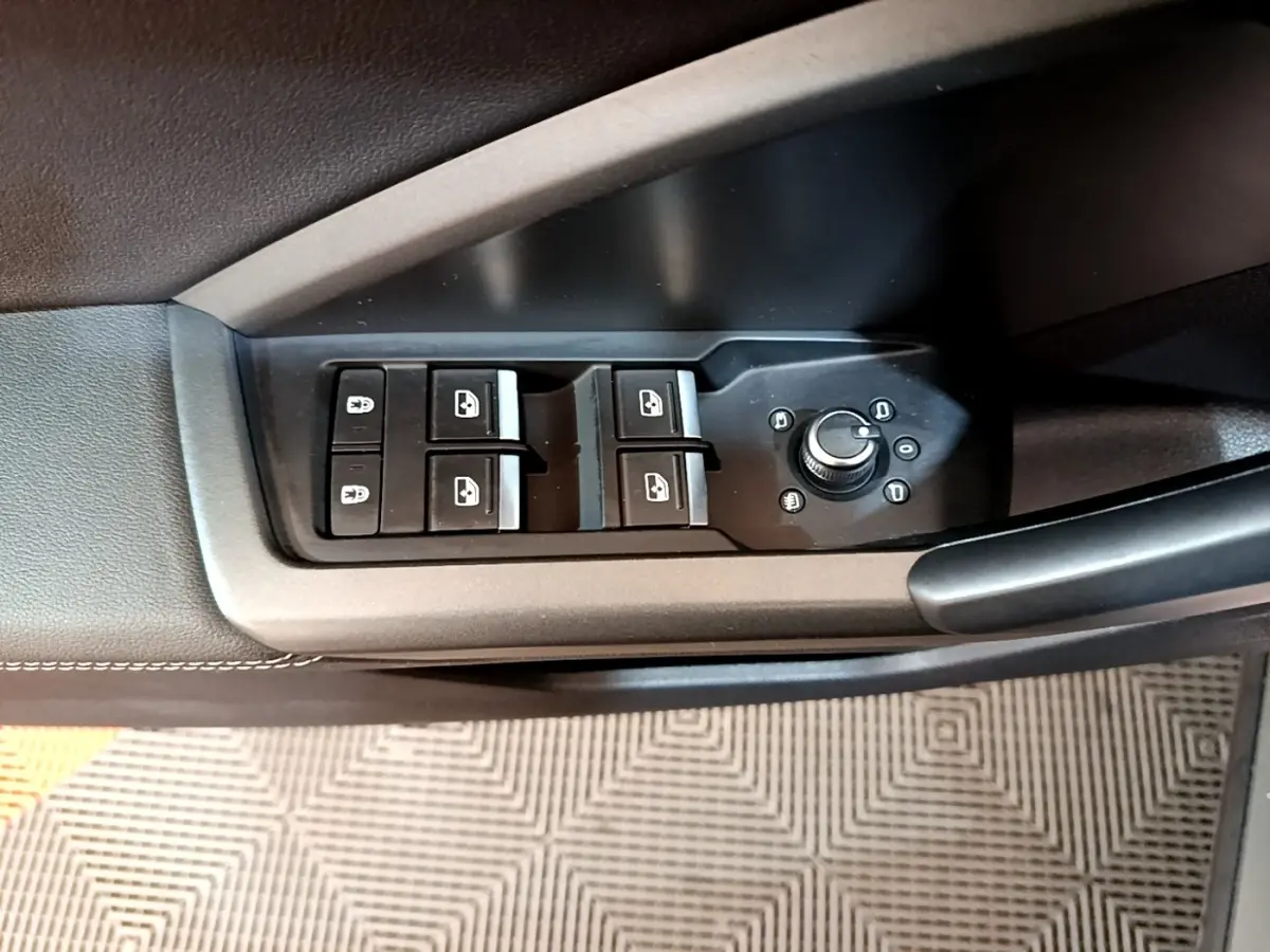 Vue rapprochée des commandes de lève-vitres et réglage des rétroviseurs sur la porte côté conducteur d’un Audi Q3 gris foncé.