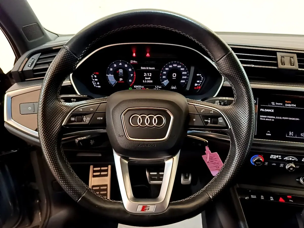 Vue centrée sur le volant cuir multifonctions de l'Audi Q3 gris foncé avec tableau de bord digital et écran tactile.
