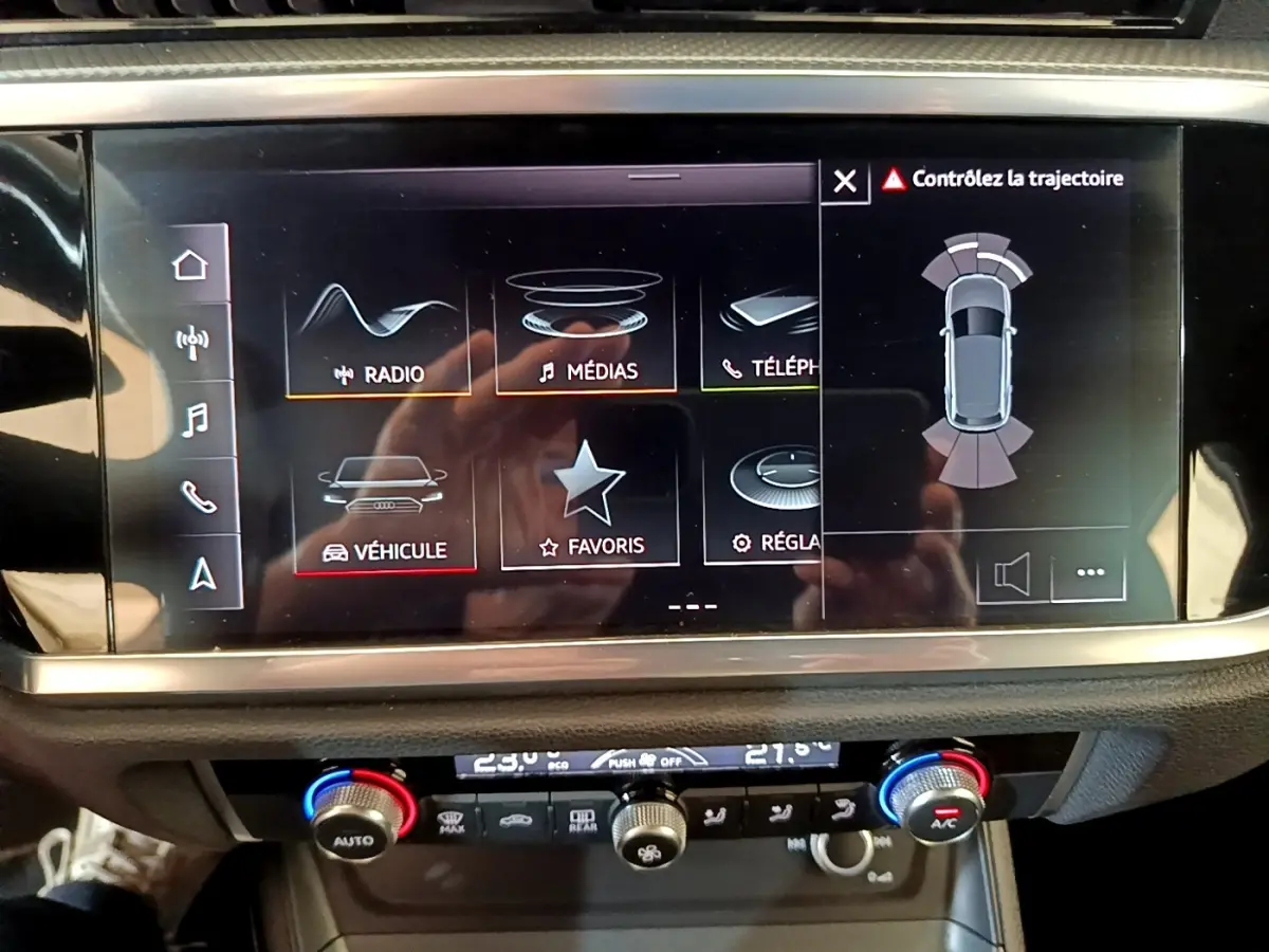 Écran tactile central affichant l'aide au stationnement et les réglages multimédias dans un Audi Q3 gris foncé.