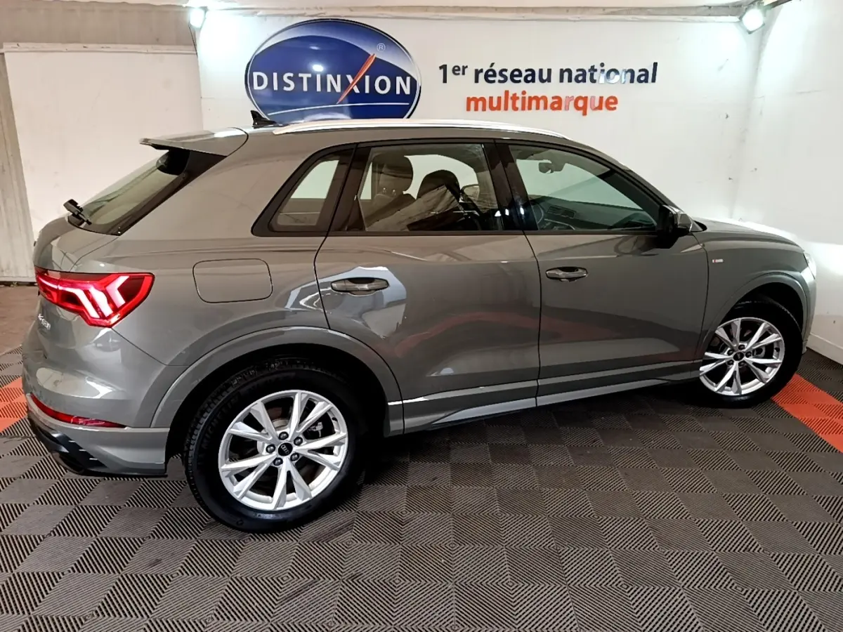 Audi Q3 gris foncé vue de profil côté droit, avec jantes alliage et feux arrière LED allumés.