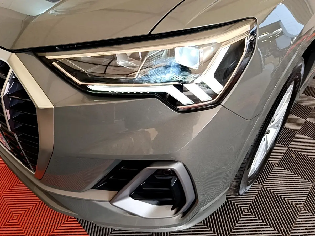 Gros plan sur le phare avant droit d’un Audi Q3 gris foncé 35 TFSI S Line avec calandre et antibrouillard visibles.