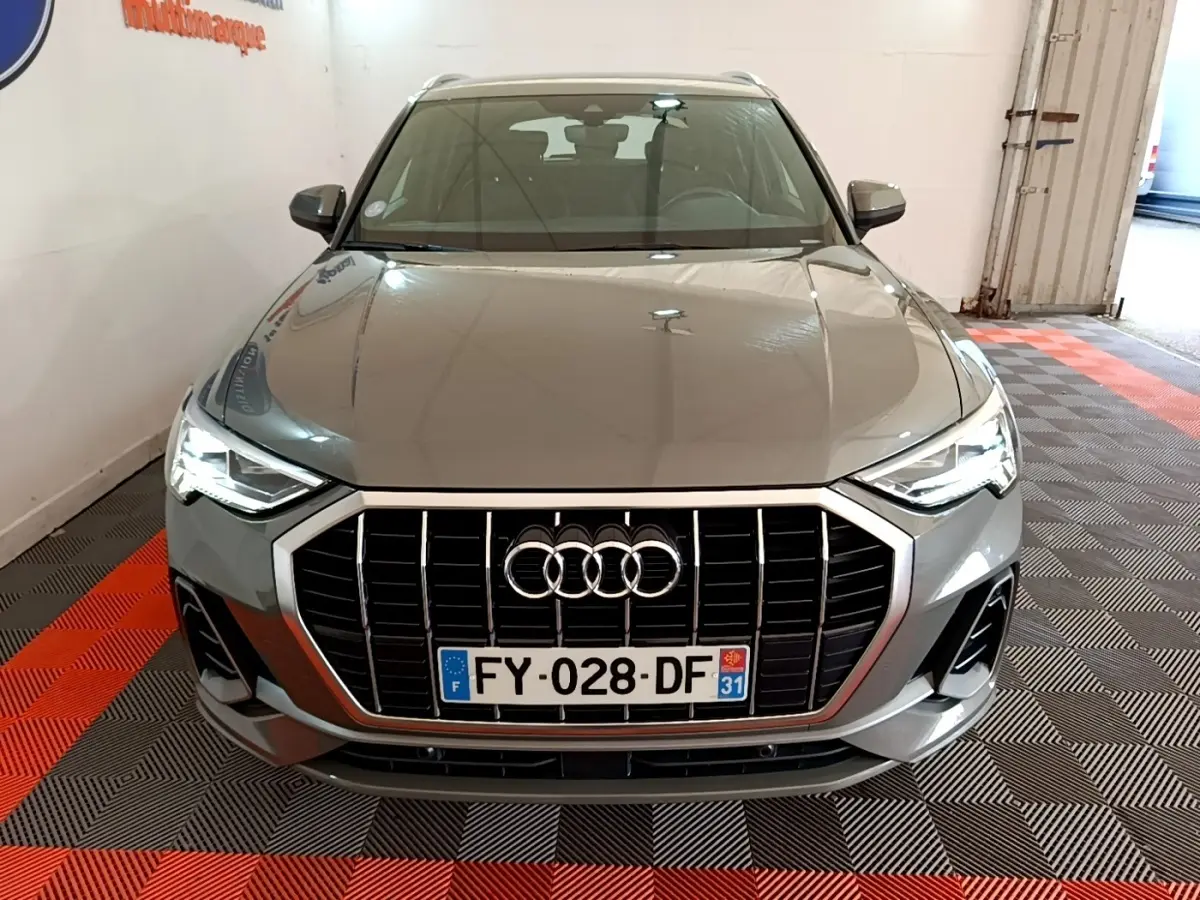 Audi Q3 gris foncé vue de face en intérieur, avec calandre large et phares LED allumés.