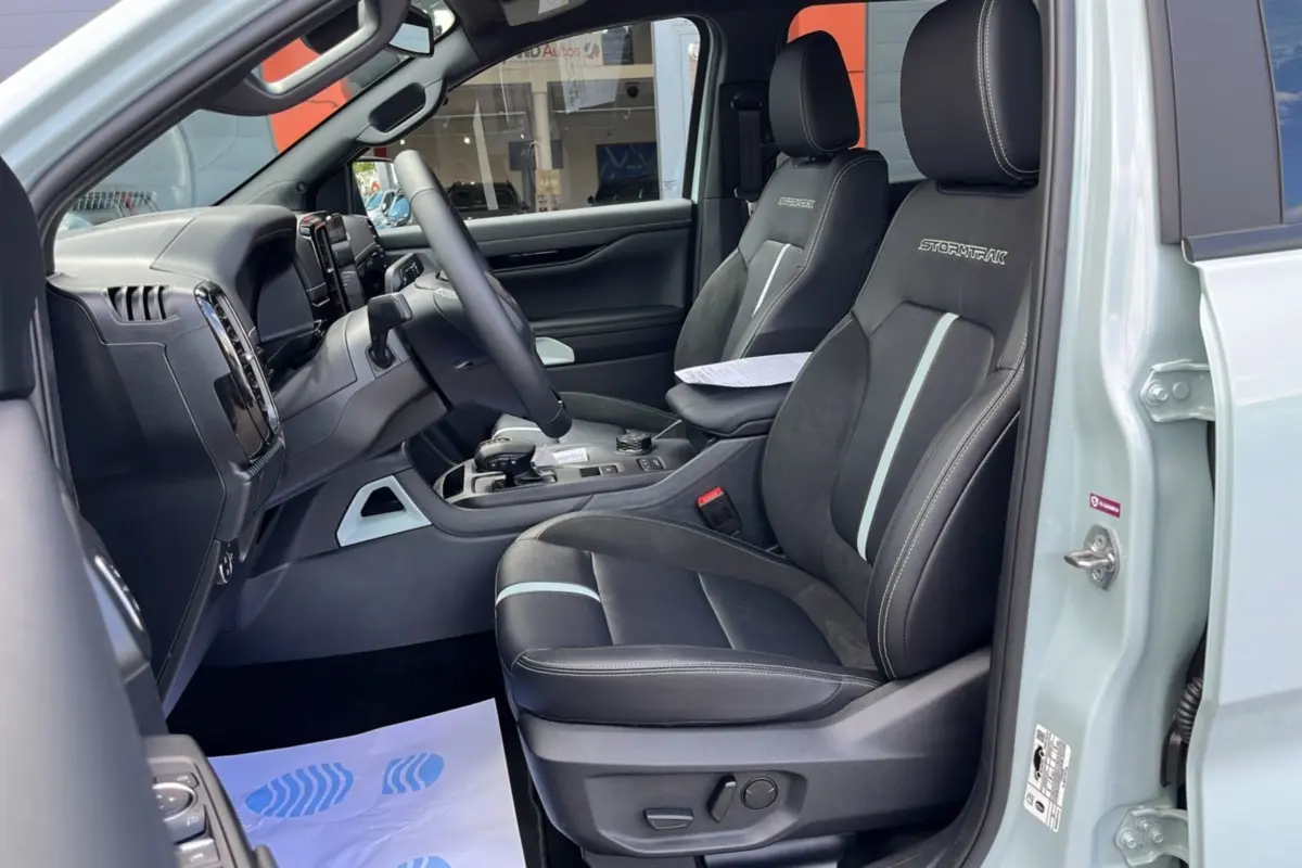 Vue intérieure côté conducteur du Ford Ranger gris zen 2026, sièges Stormtrak noirs avec surpiqûres blanches et volant multifonctions.