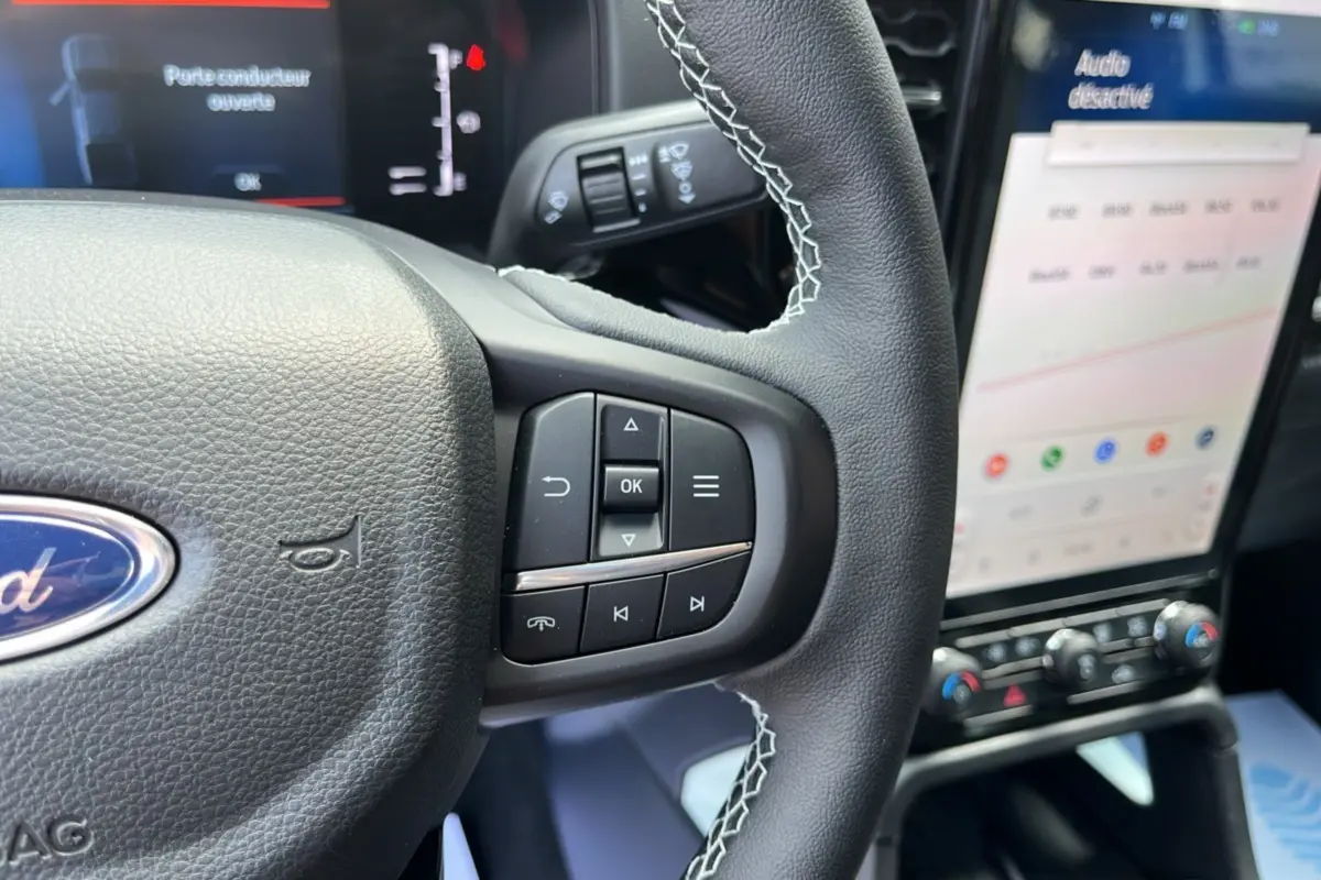 Gros plan sur le volant cuir multifonctions avec coutures blanches du Ford Ranger 2.3 PHEV 281 STORMTRAK, écran tactile en arrière-plan.
