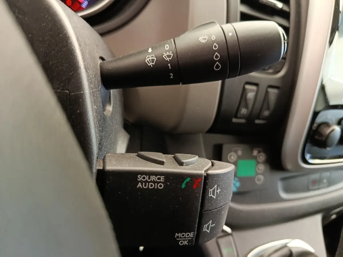 Gros plan sur la commande audio au volant du Renault Trafic Fourgon blanc, avec levier d’essuie-glace en arrière-plan.