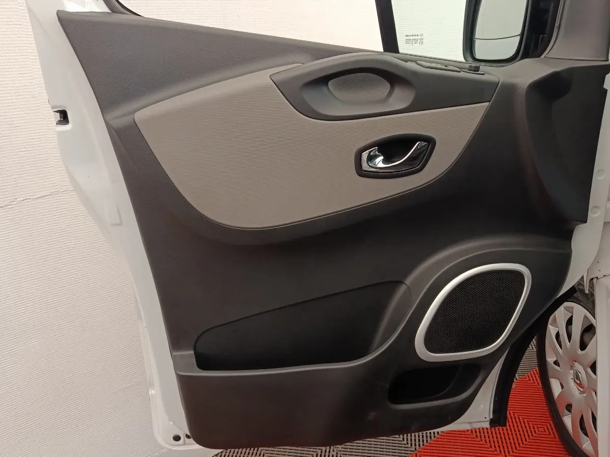 Vue rapprochée de la porte avant gauche blanche du Renault Trafic Fourgon avec poignée chromée et haut-parleur intégré.