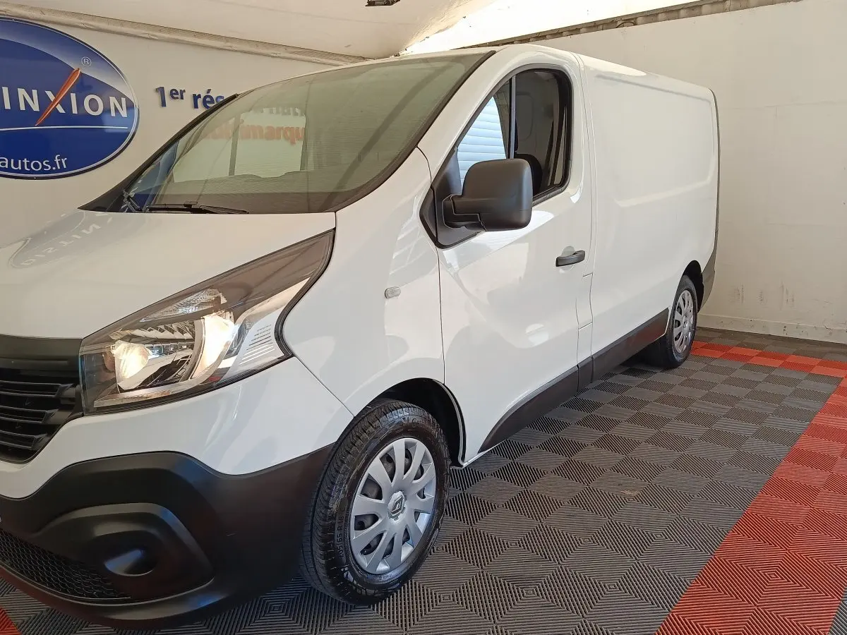 Renault Trafic Fourgon blanc vu en 3/4 avant droit, avec phares allumés et jantes acier grises.
