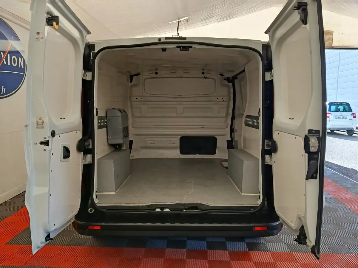 Vue arrière du fourgon Renault Trafic blanc 2017 avec portes ouvertes montrant l'espace de chargement vide et cloison pleine.