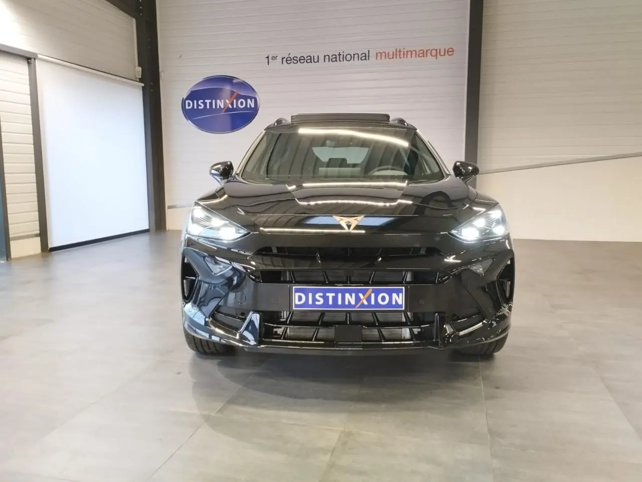 Vue frontale d'un CUPRA Formentor noir métal 2026 avec logo CUPRA doré et phares Full LED allumés en intérieur showroom.
