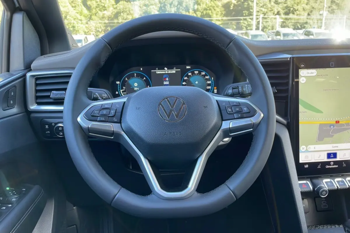 Vue rapprochée du volant multifonction noir du Volkswagen Amarok Simple Cabine 2025 avec tableau de bord numérique et écran tactile.