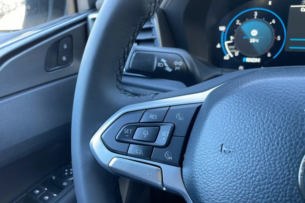 Gros plan sur le volant noir du Volkswagen Amarok 2025, montrant les commandes multifonctions côté gauche et le tableau de bord numérique.