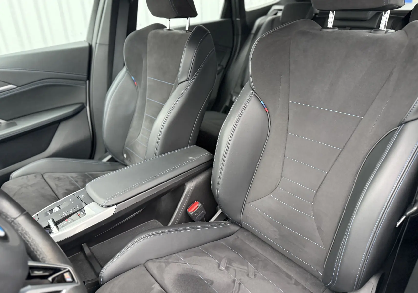 Intérieur BMW X1 18D M Sport 2025, vue rapprochée des sièges avant en cuir et alcantara noir avec surpiqûres bleues.