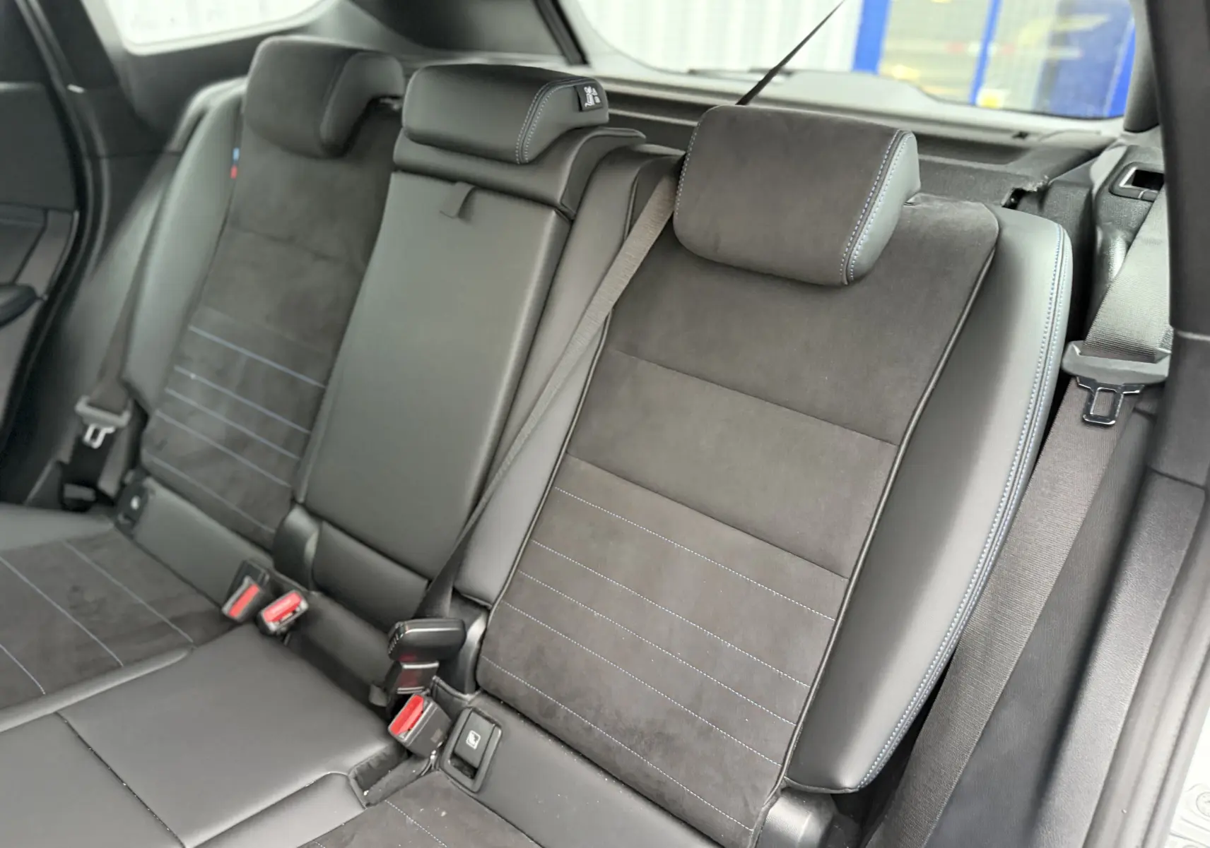 Vue rapprochée des sièges arrière en cuir noir avec surpiqûres bleues du BMW X1 18D M Sport blanc minéral 2025.