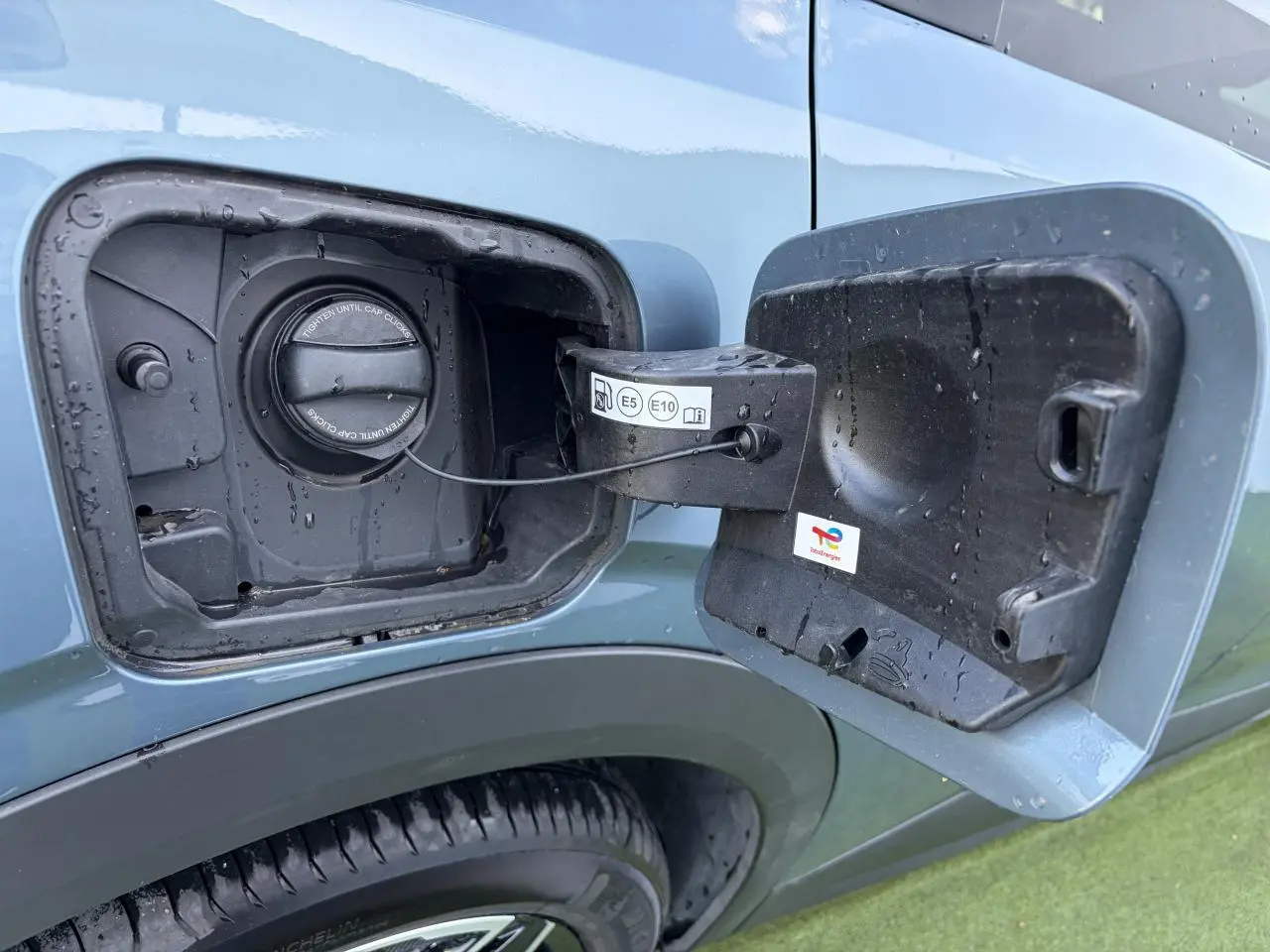 Gros plan sur la trappe à carburant ouverte côté gauche d’un Peugeot 3008 bleu Ingaro avec bouchon essence visible.