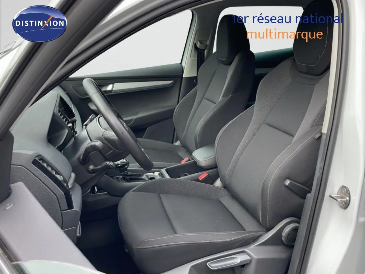 Vue intérieure côté conducteur du Skoda Karoq blanc glacier 2025, sièges tissu gris et volant multifonction.