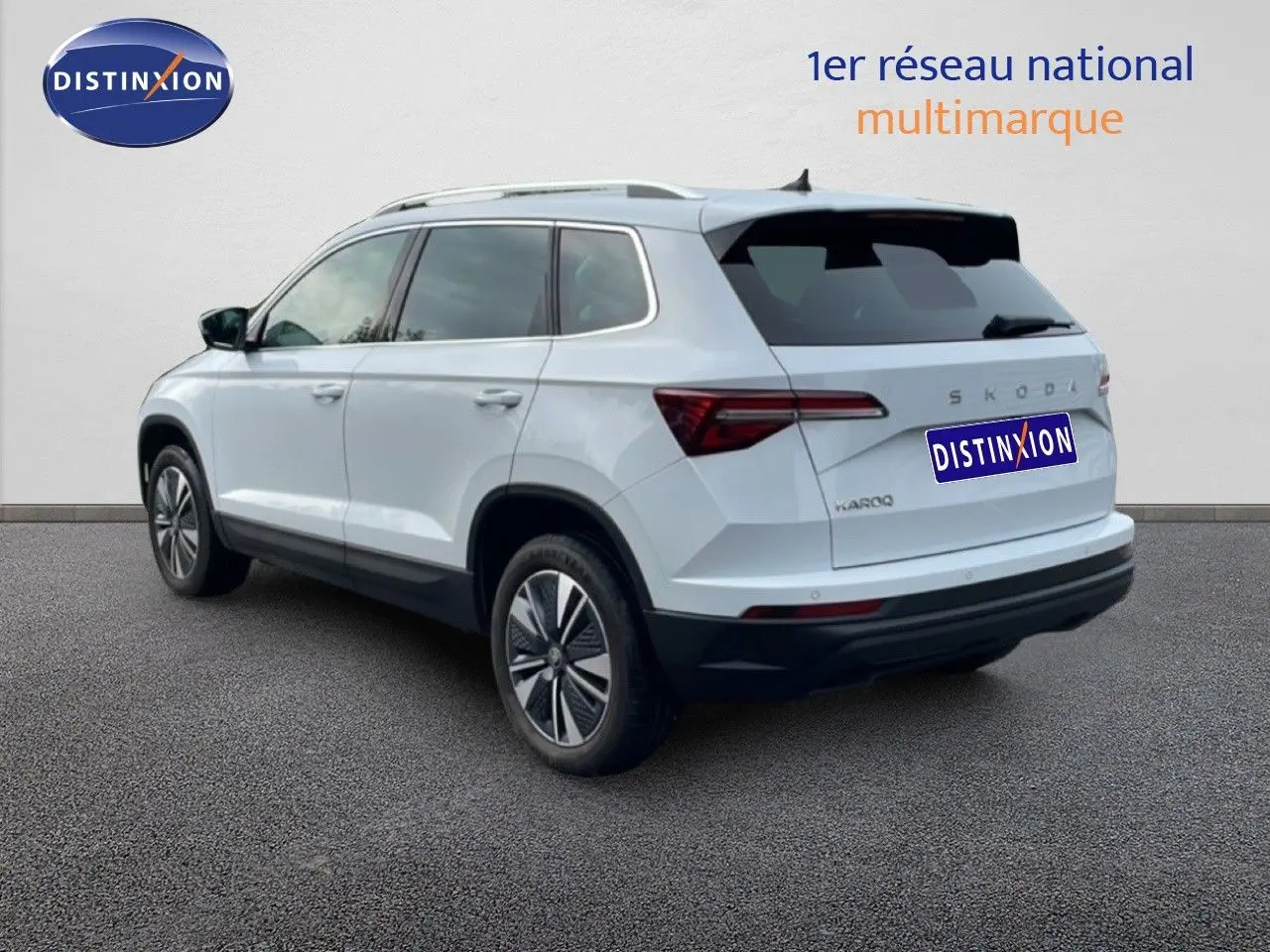 Vue 3/4 arrière droite d’un Skoda Karoq blanc glacier avec jantes bi-ton et vitres teintées.