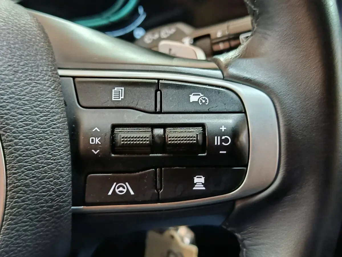 Gros plan sur les commandes du volant en cuir du Kia Sportage blanc, version hybride rechargeable 2022.