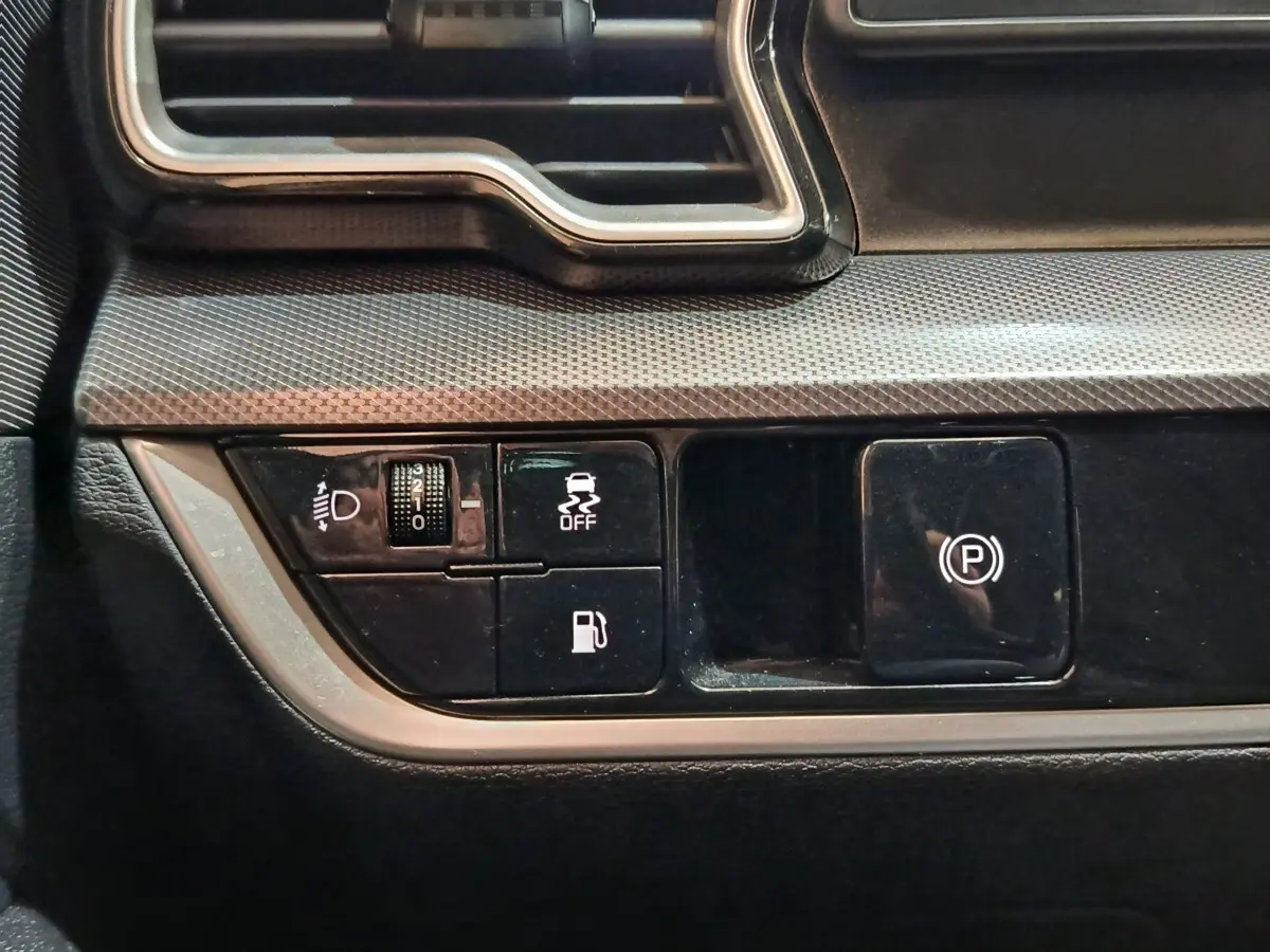 Gros plan sur les commandes de tableau de bord noir du Kia Sportage blanc, avec bouton frein à main électrique et réglage phares.