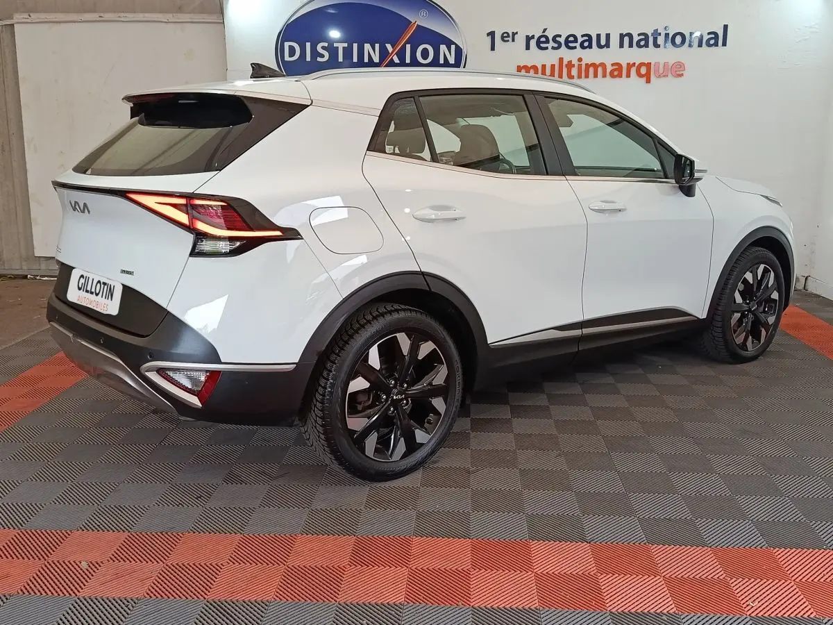 Vue 3/4 arrière droite d'un KIA Sportage blanc 2022 avec jantes noires et feux arrière LED allumés.