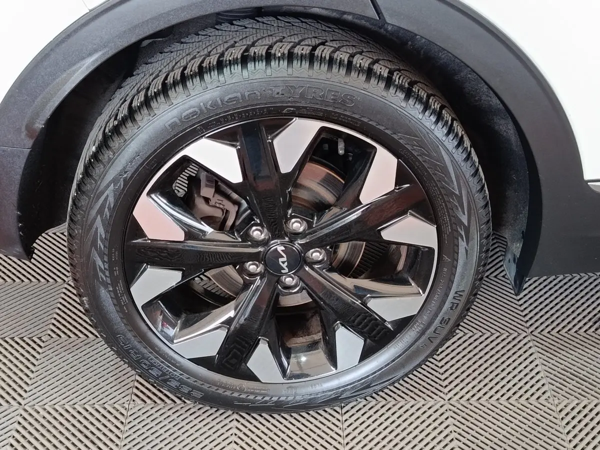 Gros plan sur la roue avant droite du KIA SPORTAGE blanc avec jante alliage noire et argentée, pneu Nokian.