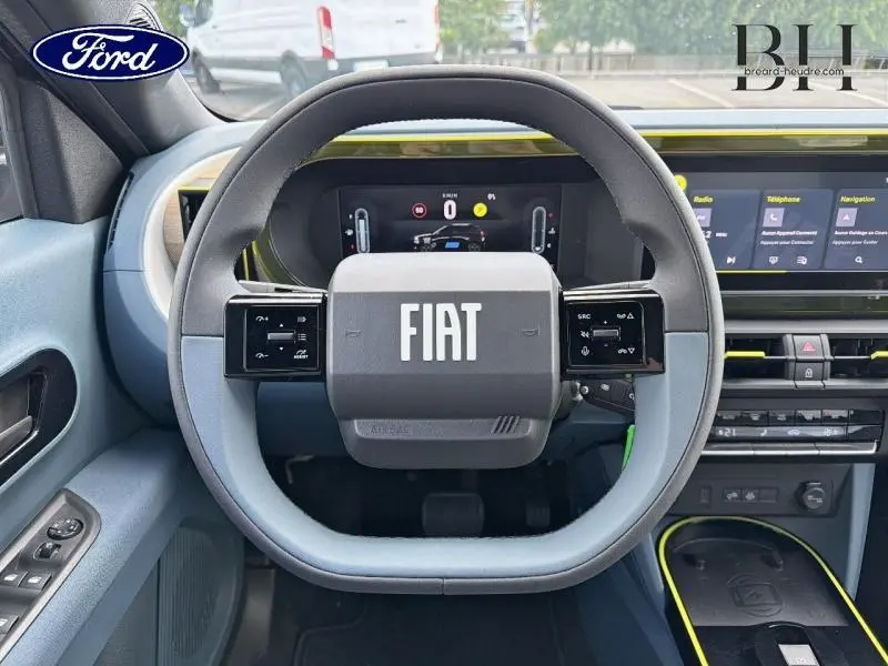 Vue intérieure centrée sur le volant bleu et noir avec logo FIAT, tableau de bord numérique et éléments jaunes contrastants.