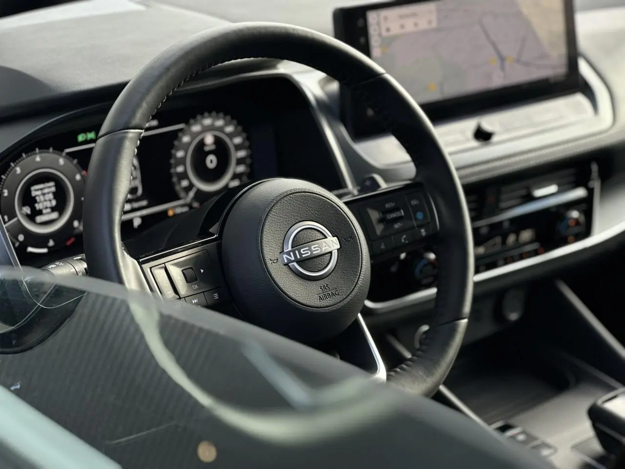 Vue rapprochée du volant cuir noir et du combiné numérique du Nissan Qashqai 2025, avec écran tactile de navigation.