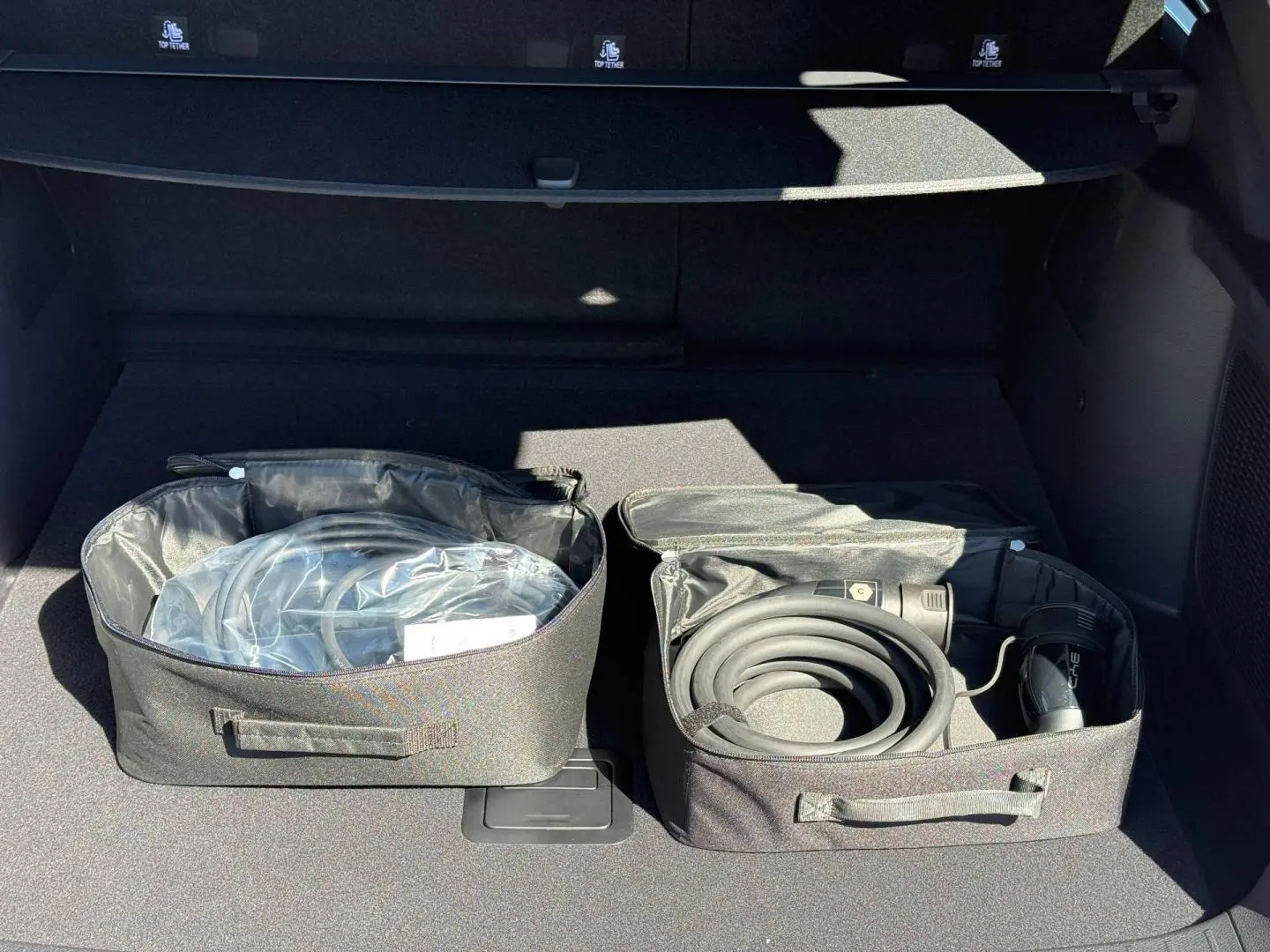 Coffre ouvert d’un BYD SEAL U 1.5 DM-i 218ch Boost avec câbles de recharge rangés dans des sacs noirs.