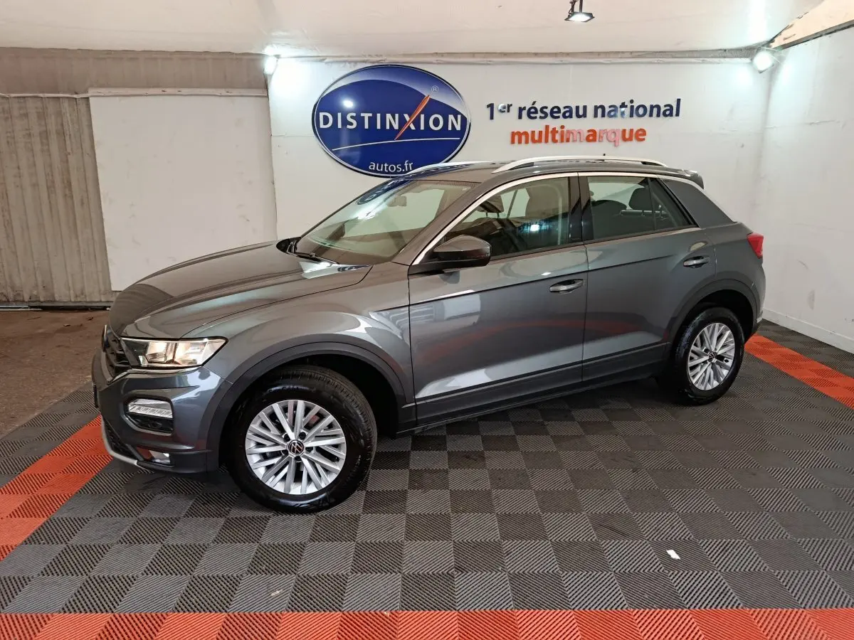 Volkswagen T-Roc gris foncé vu de profil côté gauche dans un showroom avec logo Distinxion en arrière-plan.