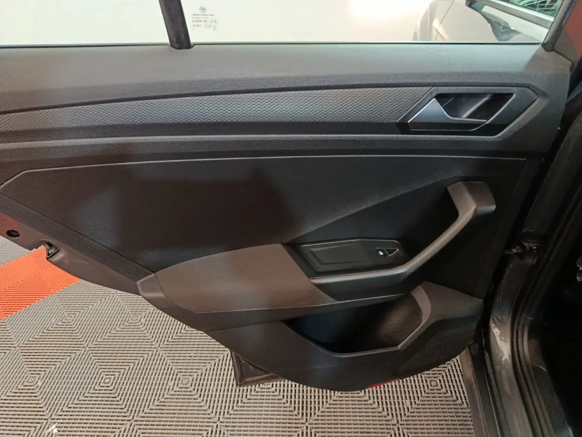 Intérieur côté gauche de la porte d'une Volkswagen T-Roc gris foncé, avec poignée et commande de vitre électrique.