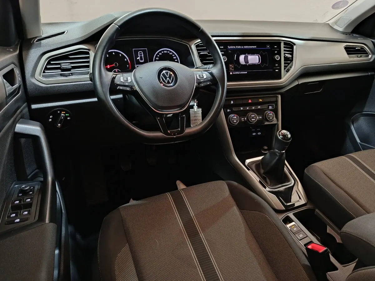 Intérieur du Volkswagen T-Roc gris foncé, vue du poste de conduite avec volant cuir et écran tactile central.