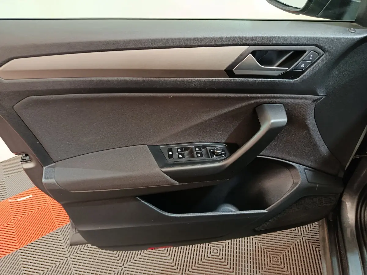 Vue rapprochée de la porte avant gauche du Volkswagen T-Roc gris foncé, montrant les commandes de vitres et la poignée noire.