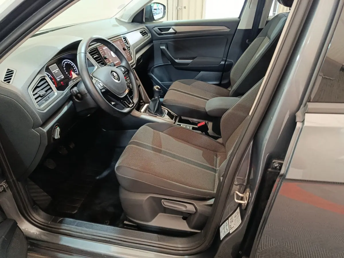Vue intérieure côté conducteur du Volkswagen T-Roc gris foncé 2021, avec volant cuir et boîte manuelle visible.