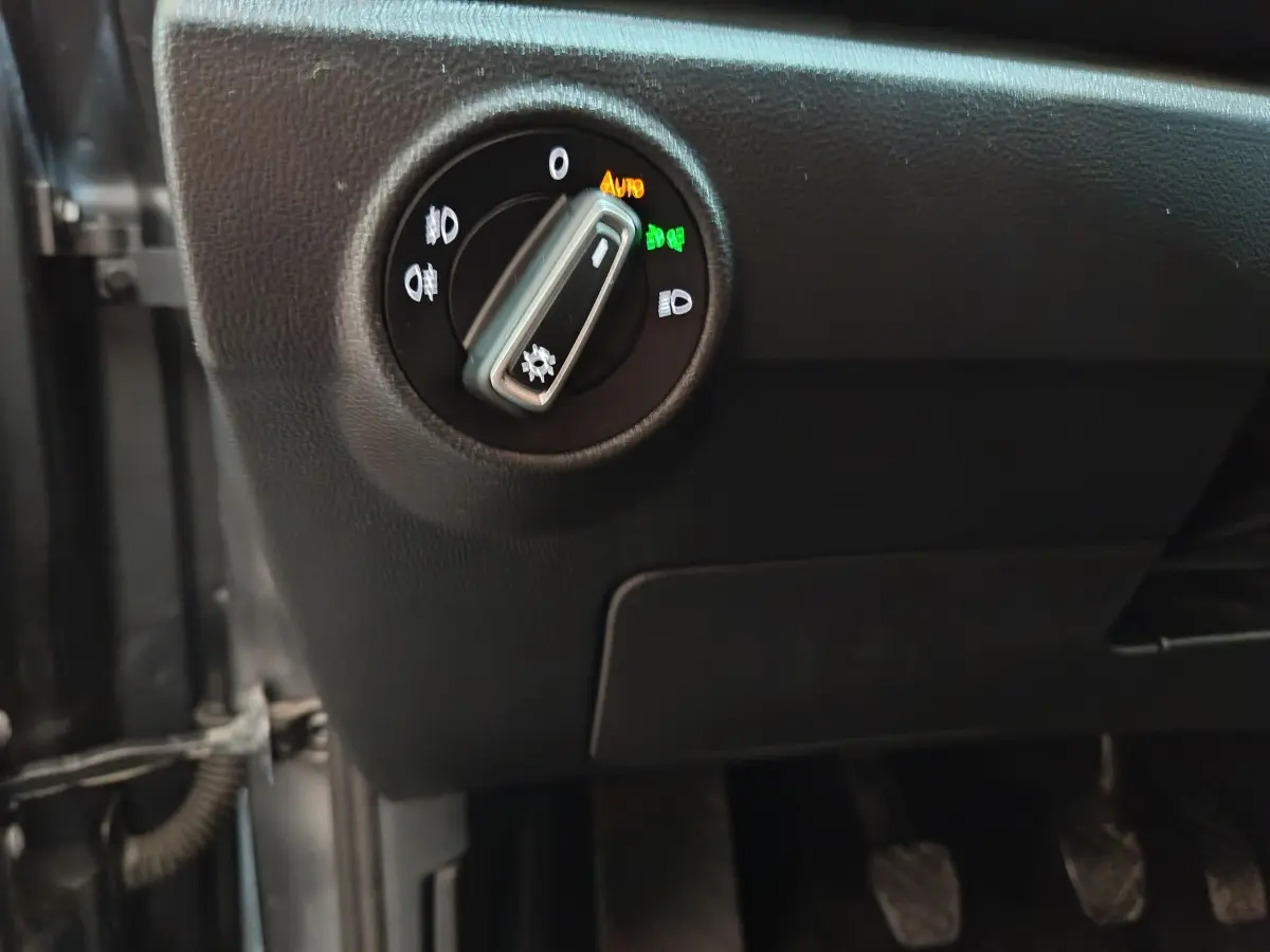 Gros plan sur le bouton de commande des phares à gauche du tableau de bord d'un Volkswagen T-Roc gris foncé.