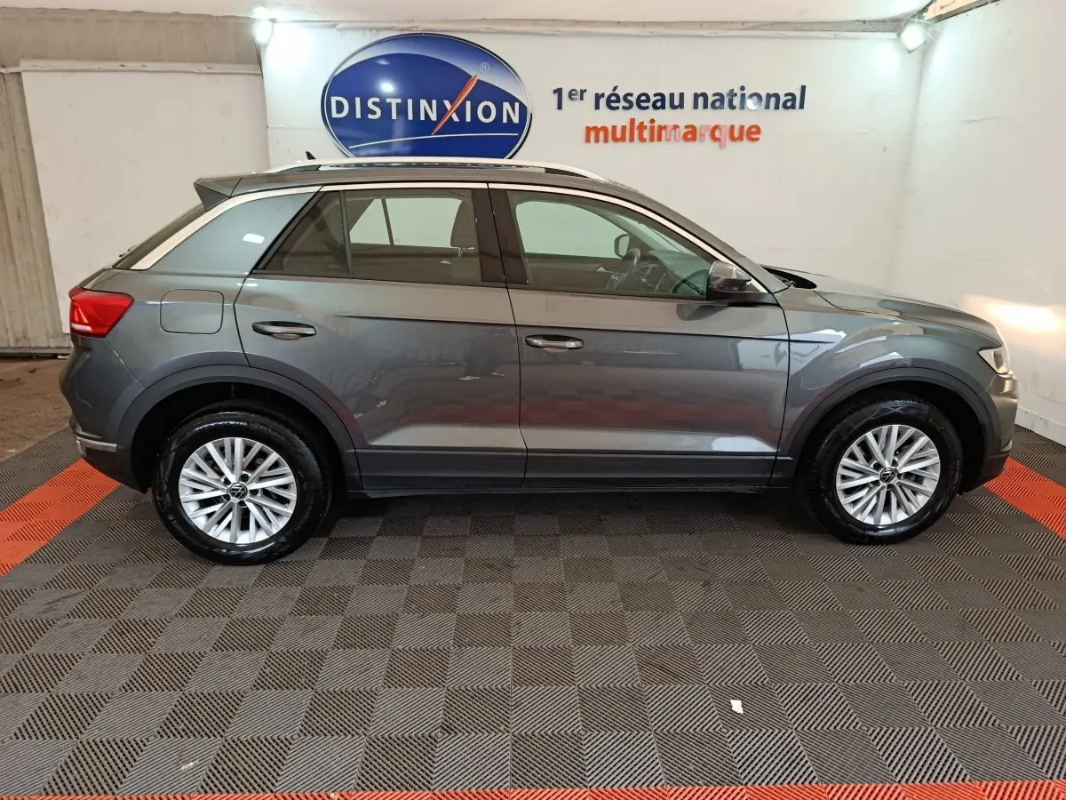 Profil côté droit d'un Volkswagen T-Roc gris foncé 2021 garé en intérieur avec jantes alliage et rails de toit noirs.
