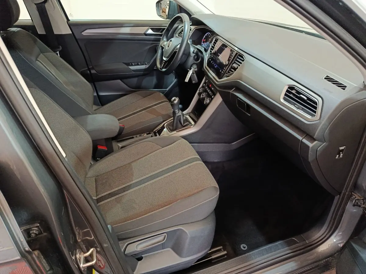 Intérieur avant droit du Volkswagen T-Roc gris foncé 2021, montrant sièges tissu, volant cuir et tableau de bord tactile.