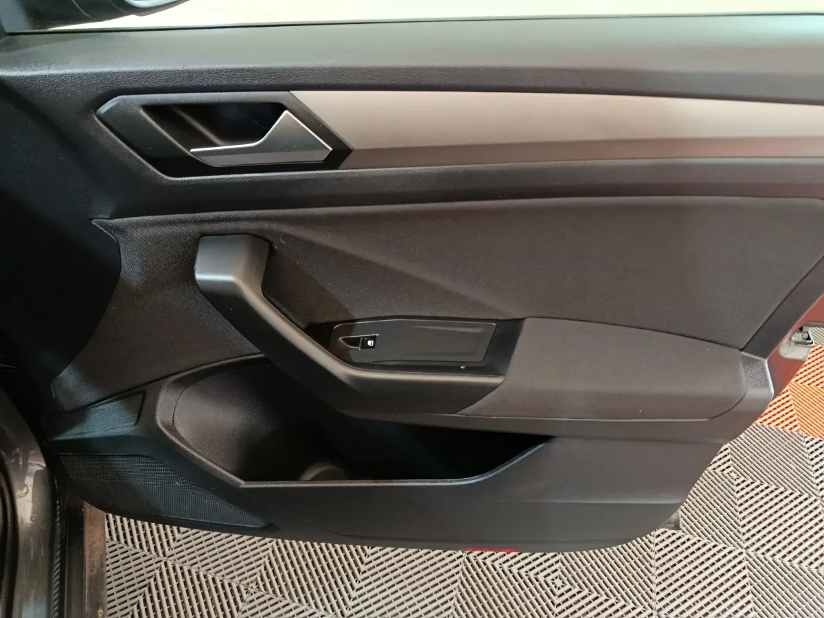 Intérieur côté gauche de la porte avant d'un Volkswagen T-Roc gris foncé, avec poignée et commandes de verrouillage.
