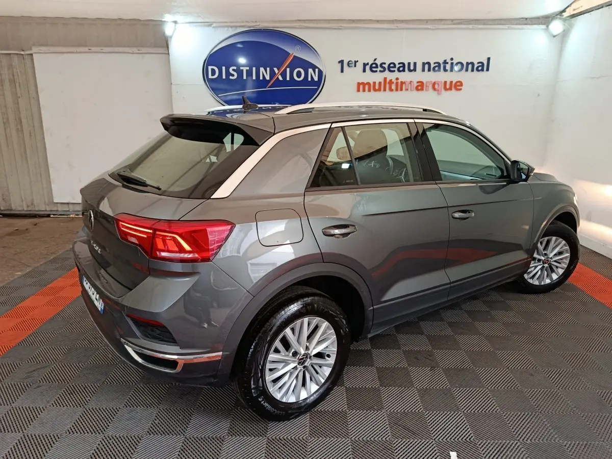 Vue 3/4 arrière droite d'un Volkswagen T-Roc gris foncé avec jantes alliage et barres de toit noires.