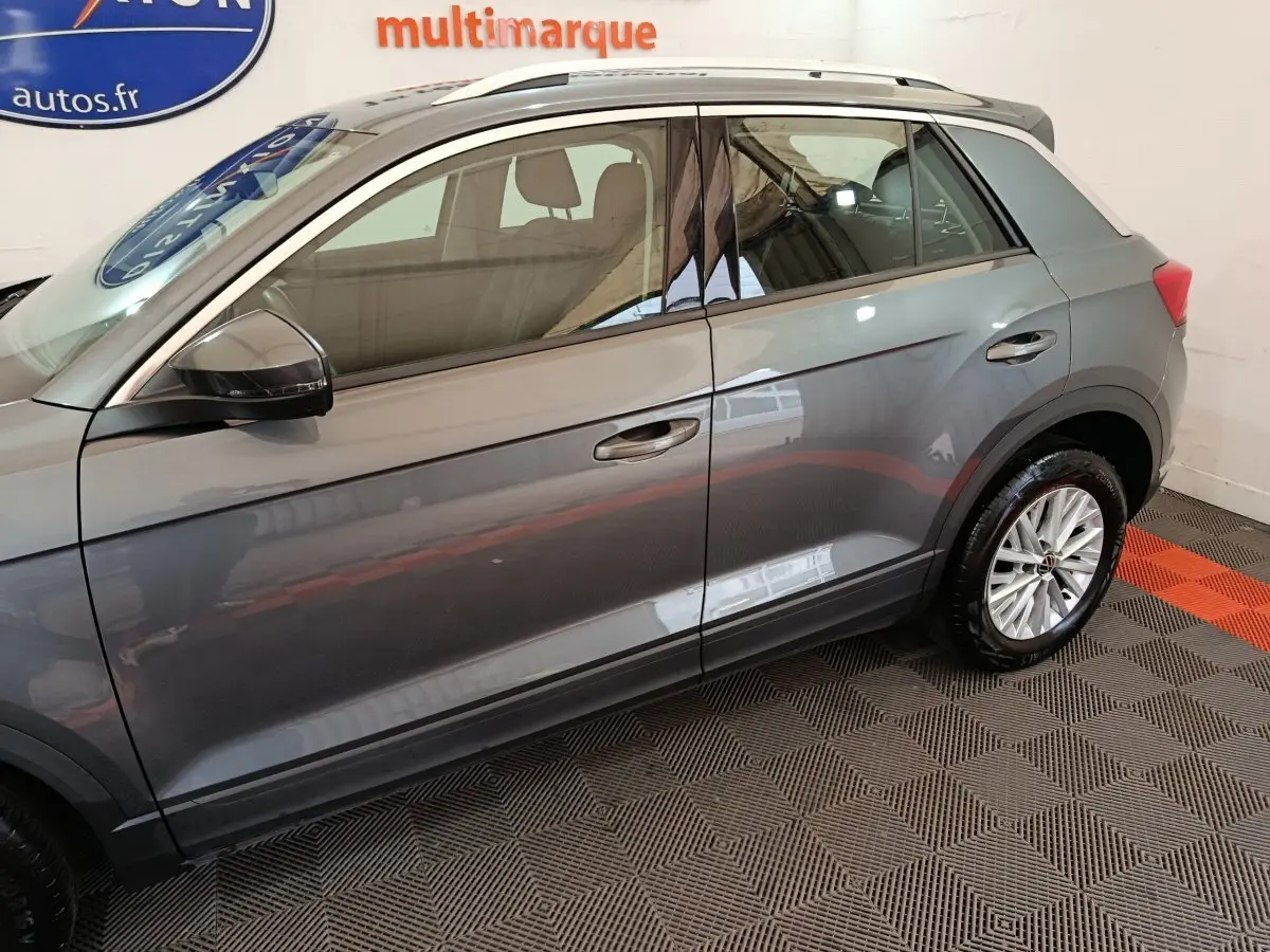 Profil côté gauche du Volkswagen T-Roc gris foncé 2021 avec jantes alliage et barres de toit noires visibles.