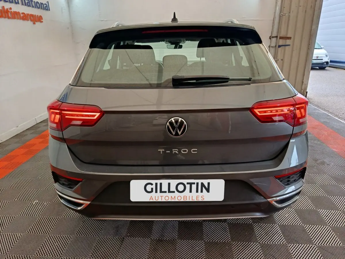 Vue arrière d'un Volkswagen T-Roc gris foncé avec feux LED et logo VW bien visibles dans un garage.