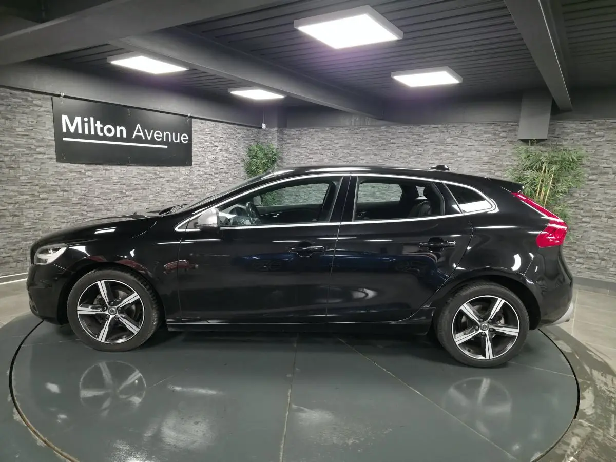 Profil côté gauche d'une Volvo V40 D2 R-Design noire métallisée avec jantes alliage Ixion 17 pouces dans un showroom.