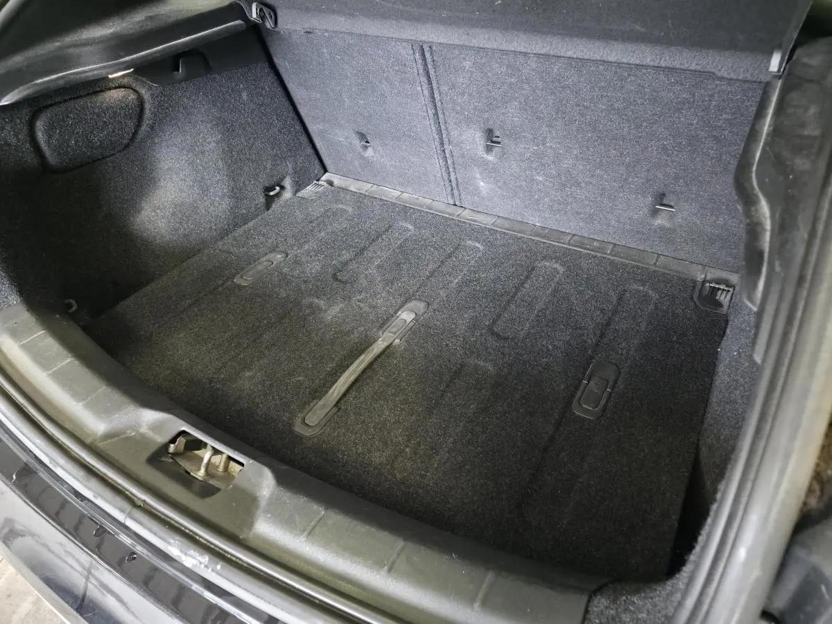 Coffre ouvert vu de dessus d'une Volvo V40 D2 R-Design noire, montrant le tapis de sol et les fixations arrière.